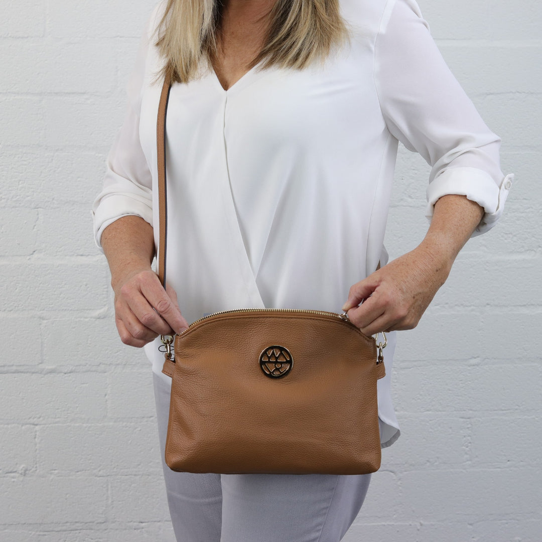 woman holding gold zip of abigail caramel leather handbag while wearing it across the body#colour_caramel