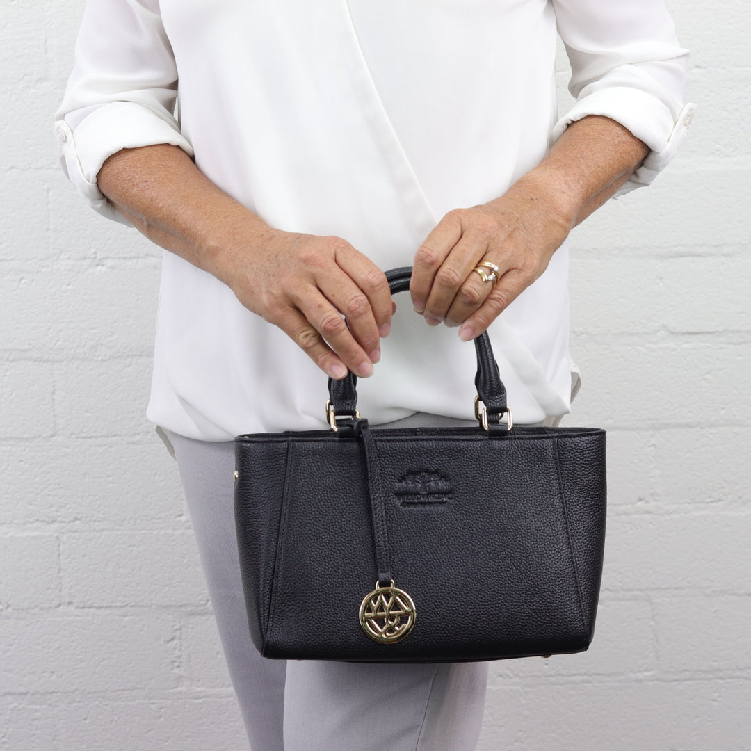 lady holding small black leather anika handbag with removable gold charm #colour_black