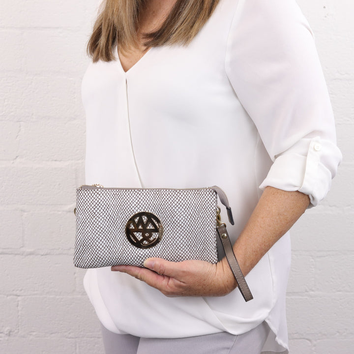 lady holding katie printed suede clutch in white and neutral brown pattern with large gold logo and included wrist strap#colour_white-fog