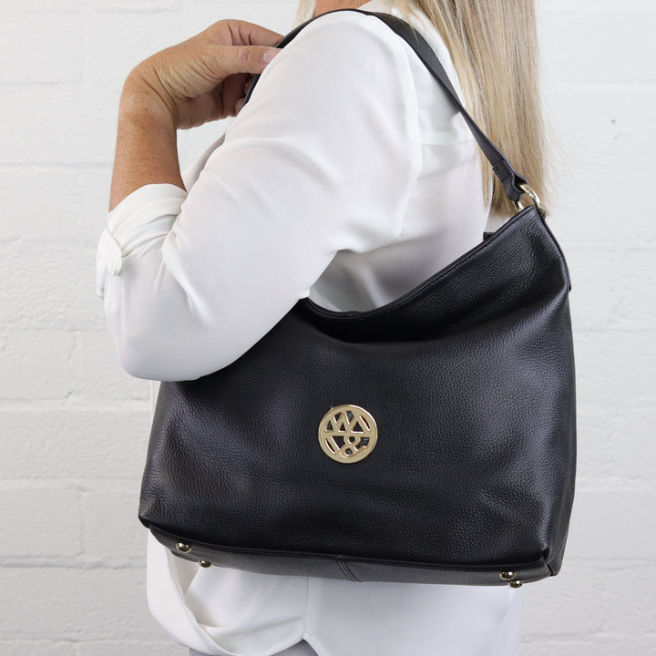 woman wearing Australian designed leather hobo handbag on shoulder in black pebbled leather with badge logo#colour_black