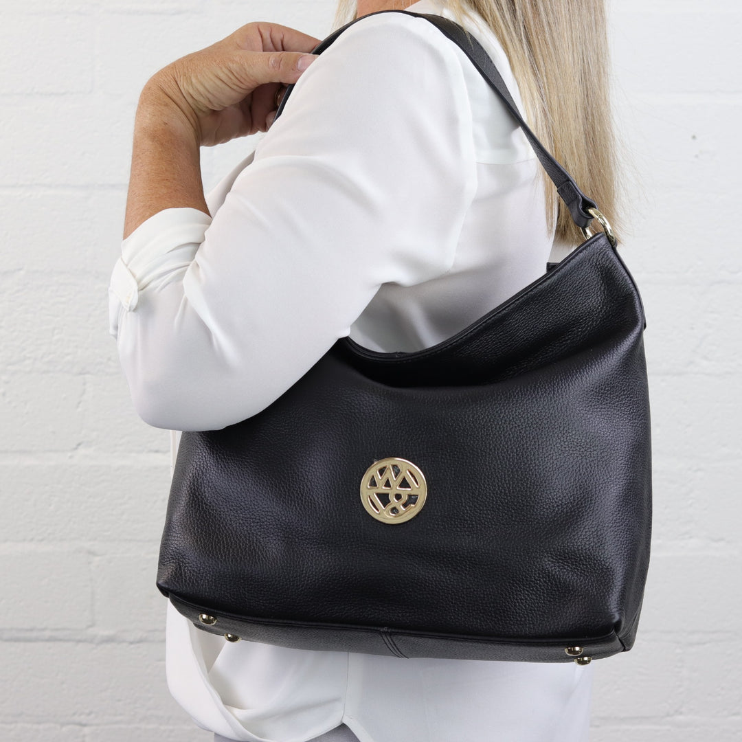 woman wearing Australian designed leather hobo handbag on shoulder in black pebbled leather with badge logo#colour_black