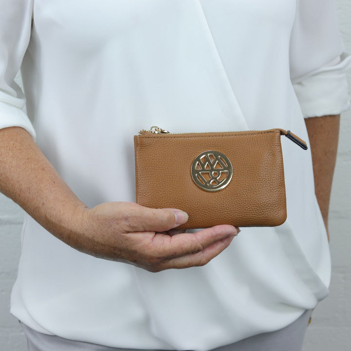 small pouch or clutch in caramel tan coloured quality pebbled leather with large badge logo being carried by woman#colour_caramel
