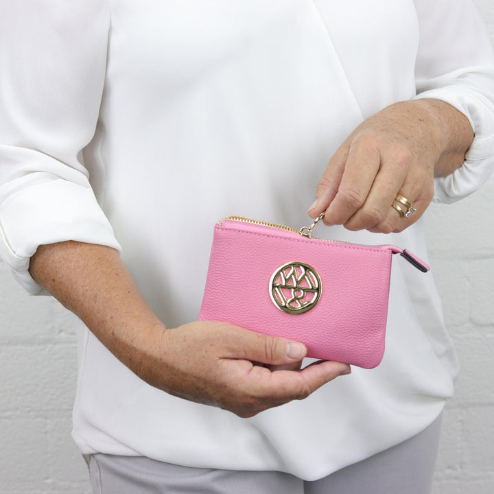 woman unzipping small purse in bright pink with gold badge logo#colour_princess-pink