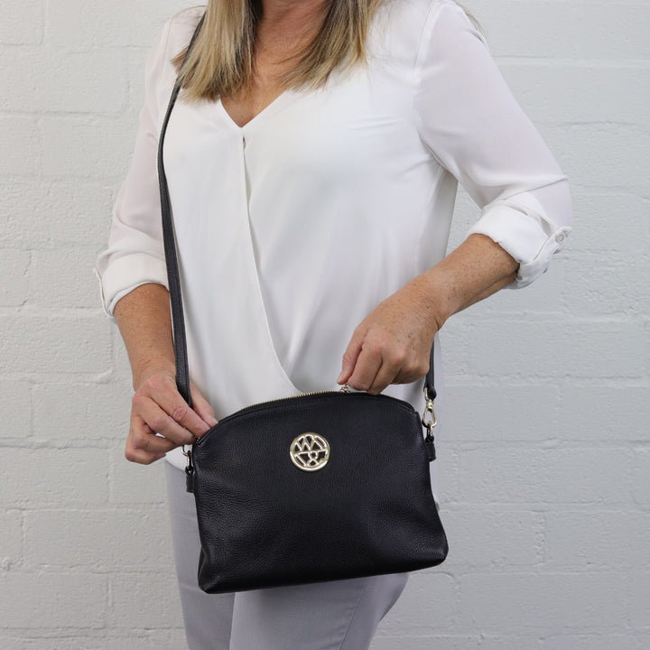 woman holding gold zip of abigail black leather handbag while wearing it across the body#colour_black