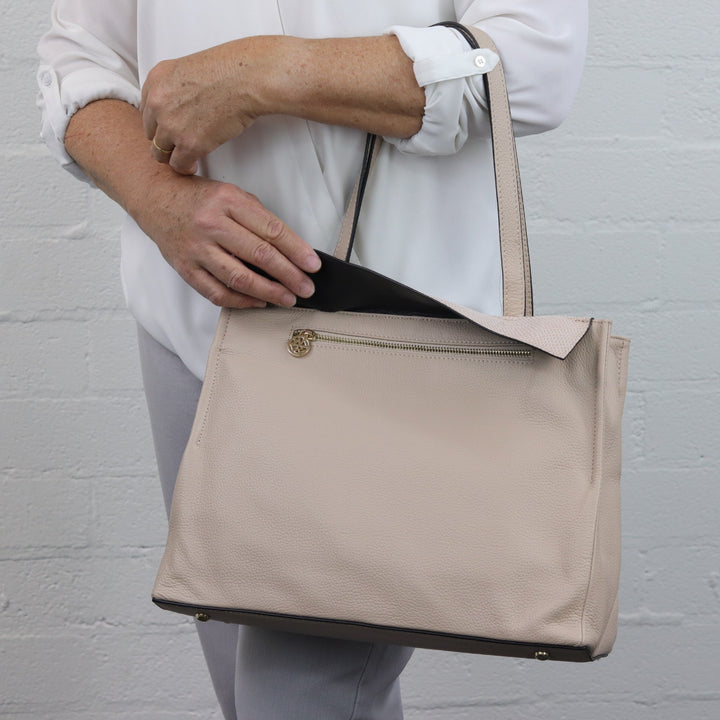 woman lifting up flap of nude colour leather tote revealing hidden zip pocket#colour_nude-with-seashell