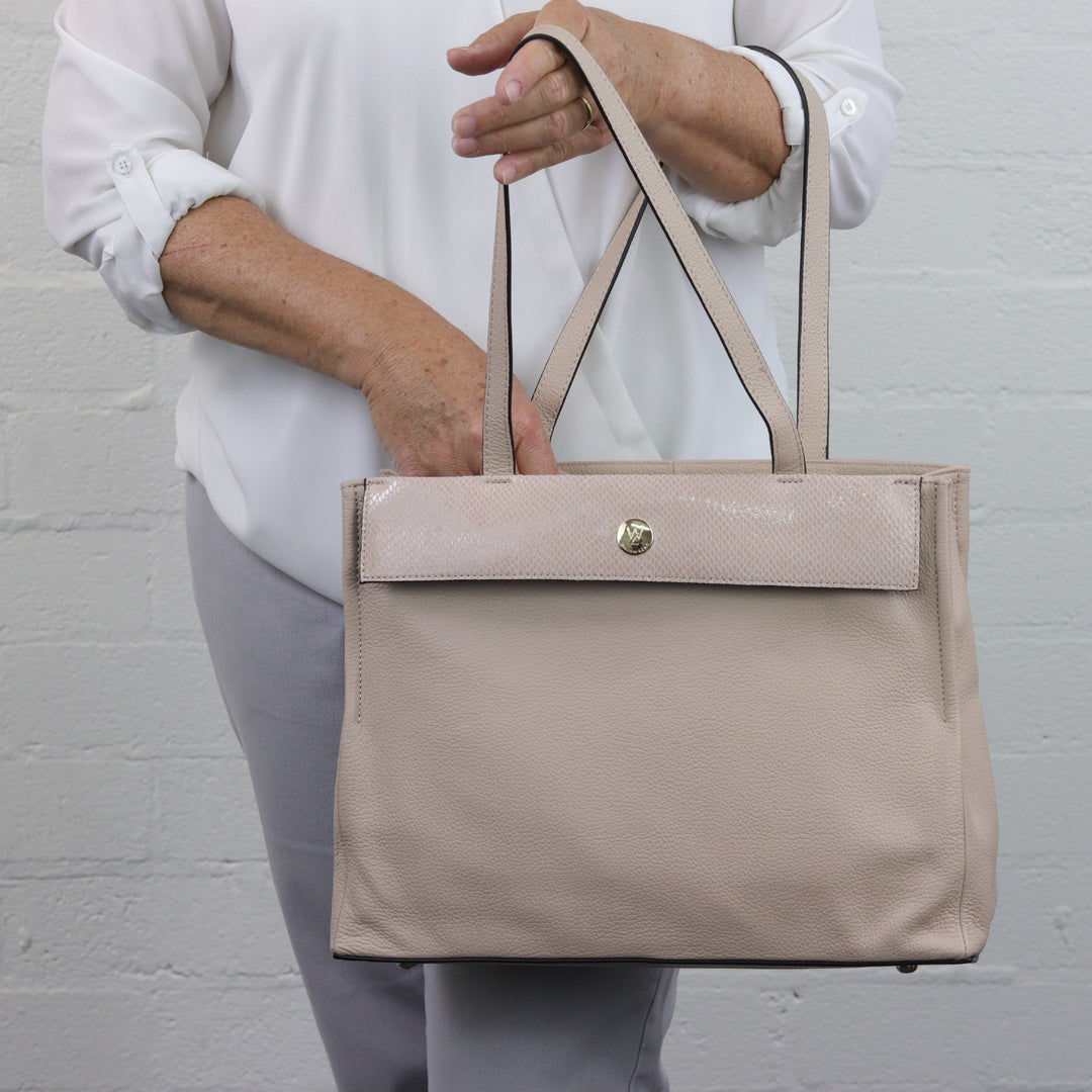 lady reaching inside of eleanor in nude pebbled leather with seashell coloured printed suede strap