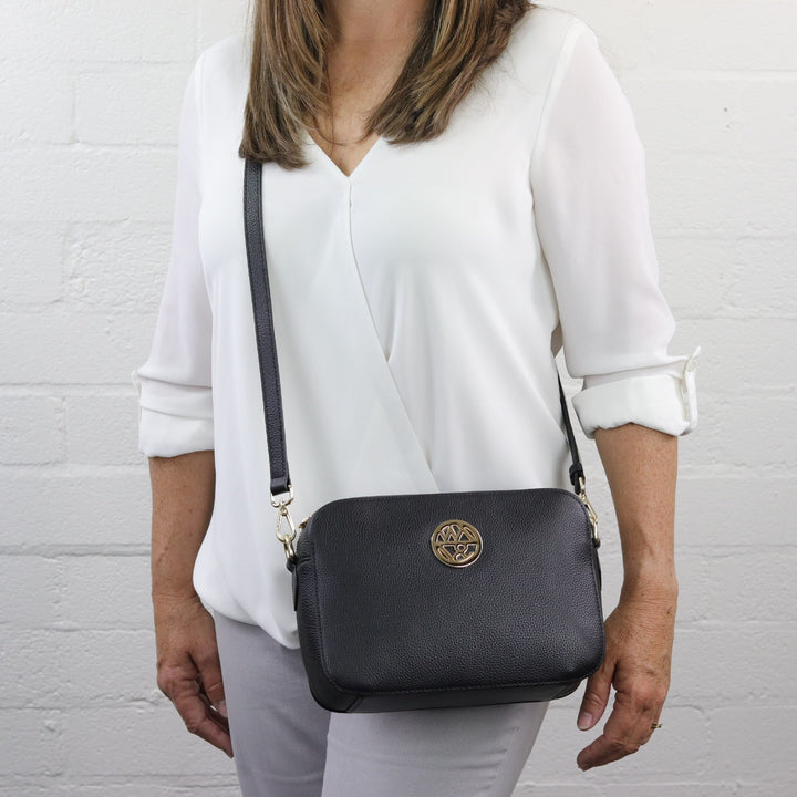 woman wearing crossbody style camera bag in black pebbled leather#colour_black