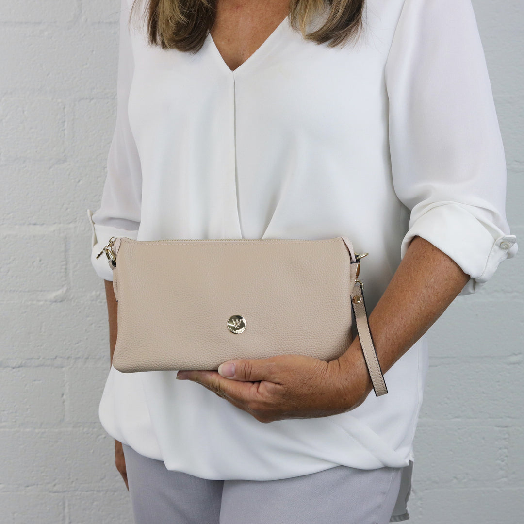 model holding gracie in nude leather as a clutch with included wrist strap#colour_nude