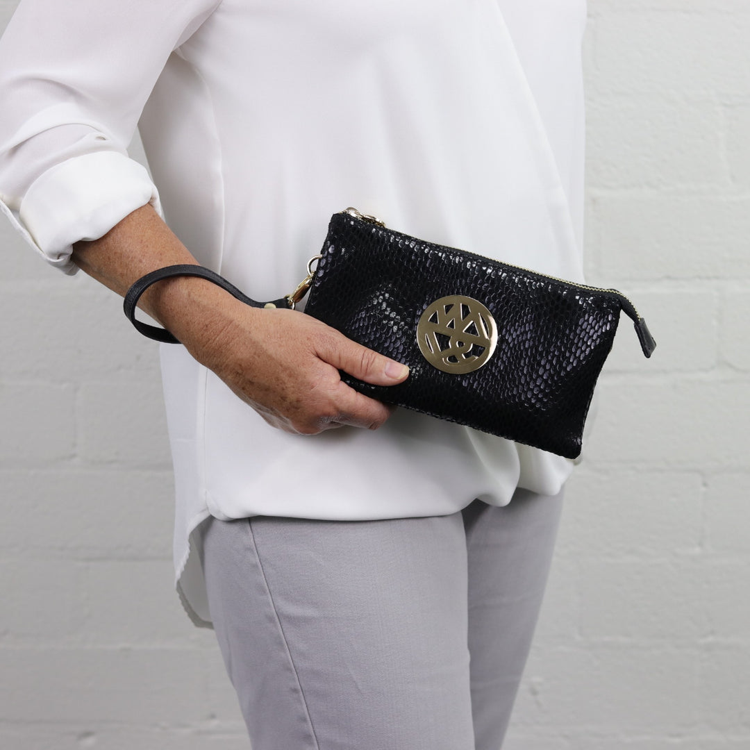 woman holding katie soft wallet clutch in jet patent black printed suede with large gold badge logo#colour_jet