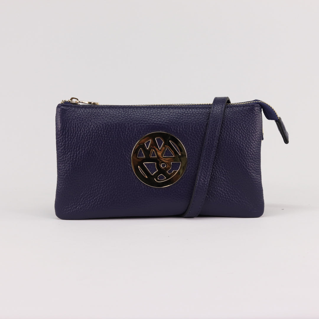 navy blue coloured soft wallet or crossbody clutch with gold badge logo and zip wrapped in adjustable long leather strap#colour_navy