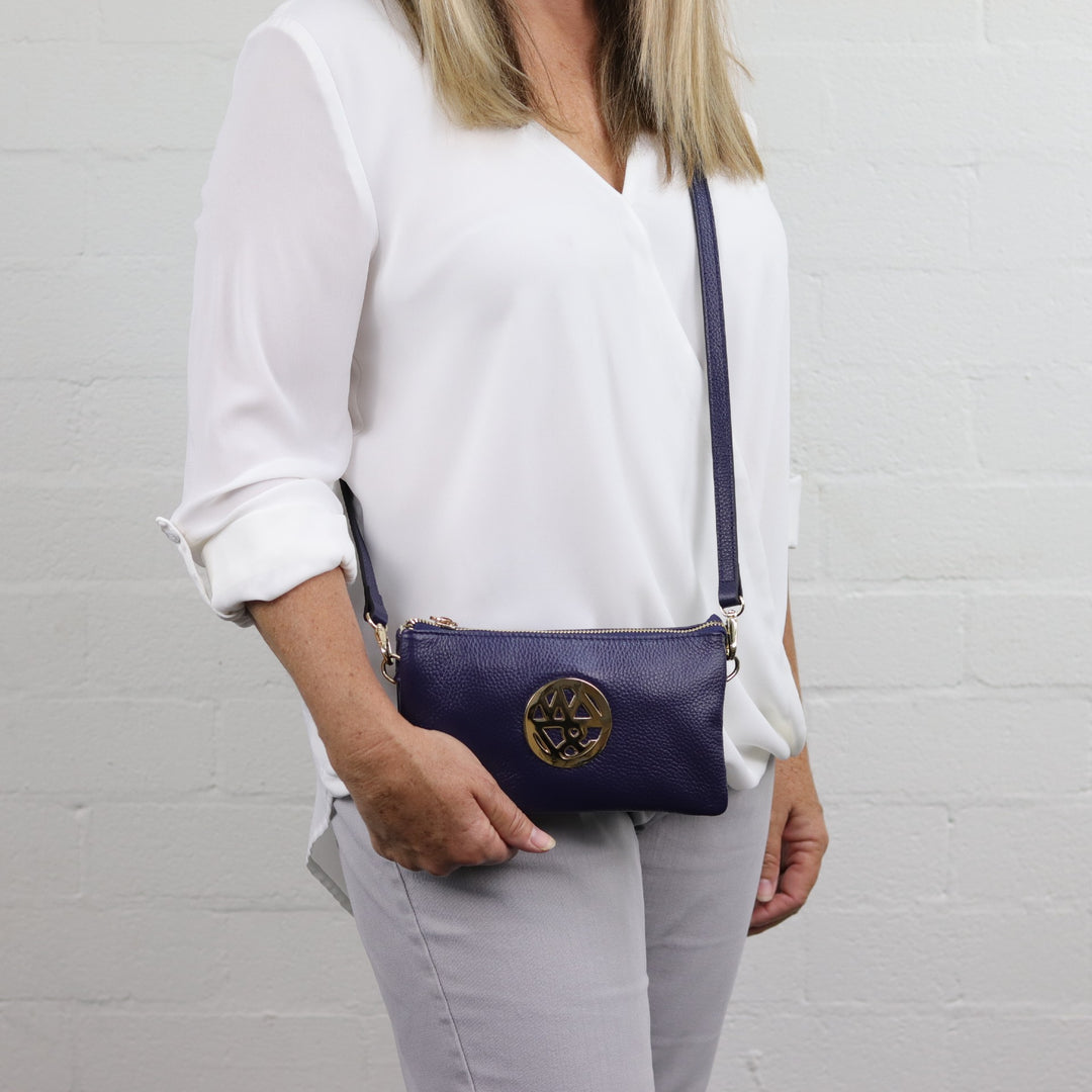 Navy blue compact handbag with gold zips and long leather strap worm crossbody#colour_navy