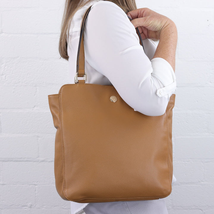 tan caramel colour portrait shape handbag with gold button logo worn on shoulder