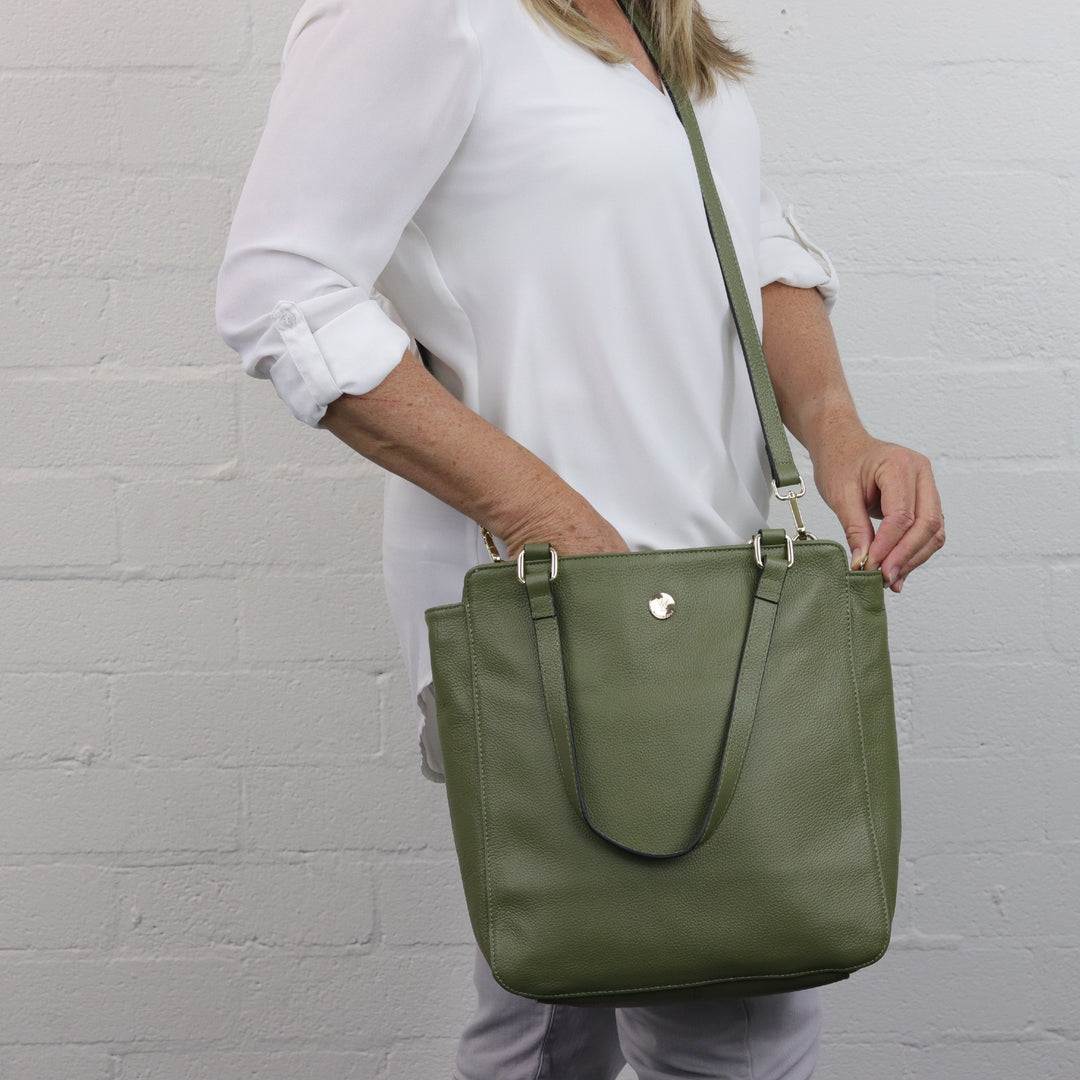 olive green coloured large bag worn with leather crossbody strap by woman