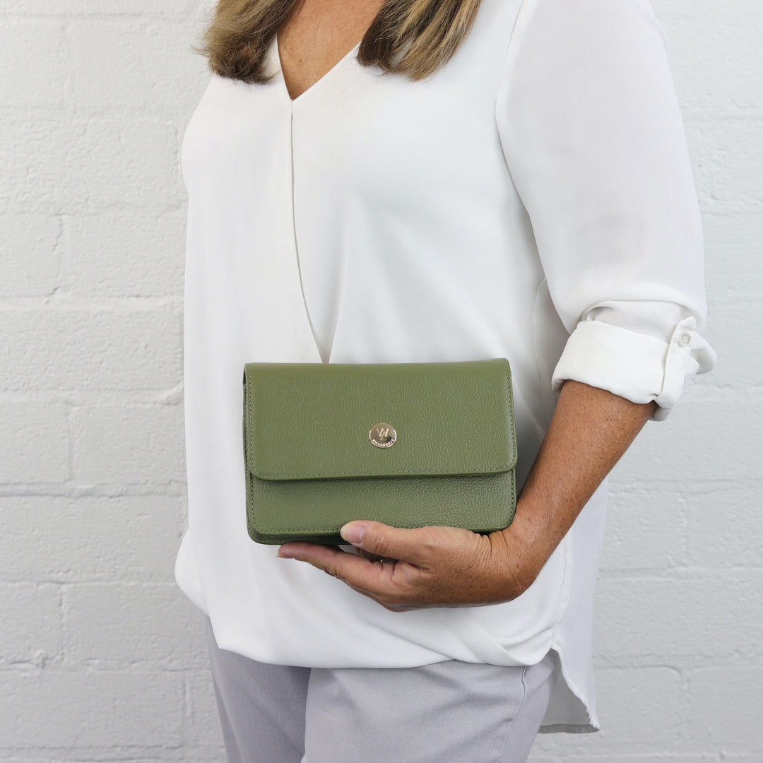 woman holding lily olive green lily leather clutch with small gold button logo#colour_olive