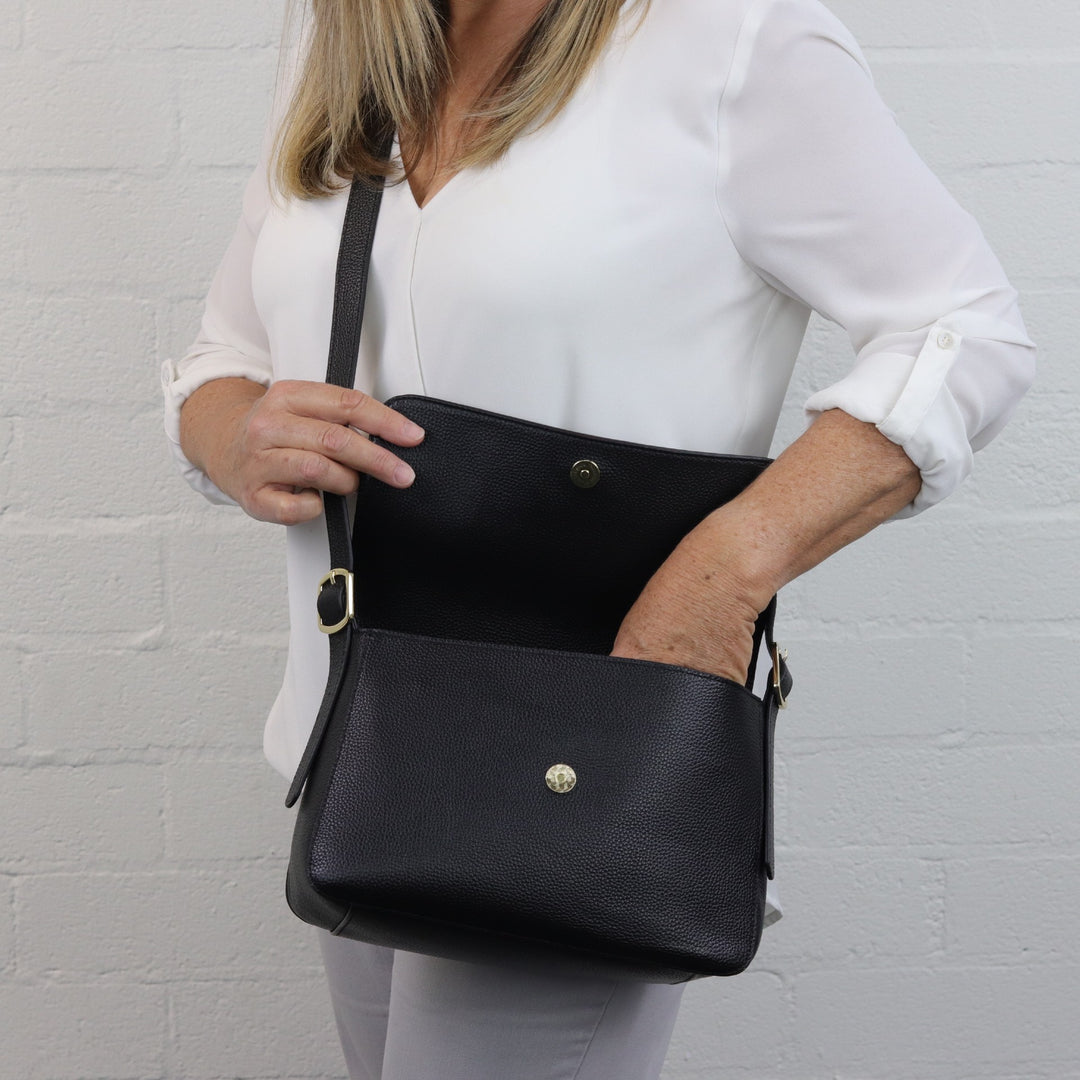woman reaching into louise crossbody bag with flap closure in black pebbled leather#colour_black