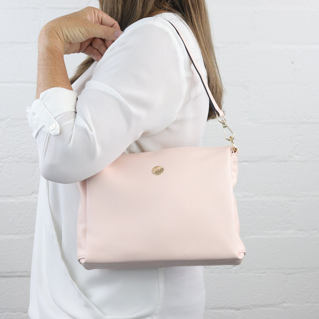 light pink nina handbag with wide base and zip closure worn on shoulder with short leather strap by lady model#colour_pink-whisper