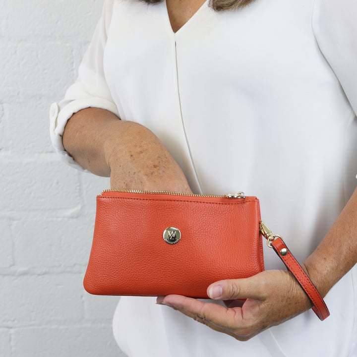 woman reaching into polly orange coloured wallet purse with gold button logo and zip closure