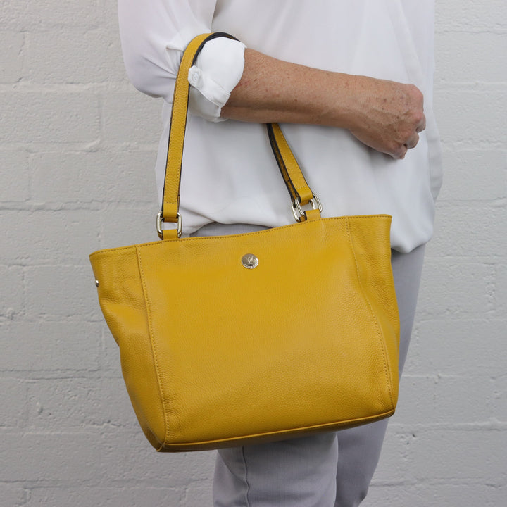 lady model wearing bright yellow bag on arm with gold button logo and zip closure
