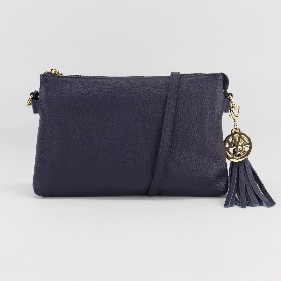 ruby versatile clutch crossbody hand bag in navy blue coloured pebbled leather with long strap and optional tassel and gold logo charm#colour_navy