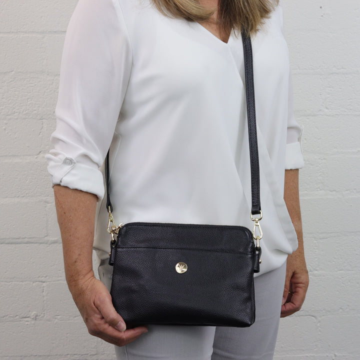 lady wearing trisha small compact shoulder bag with front slip pocket and gold button logo#colour_black