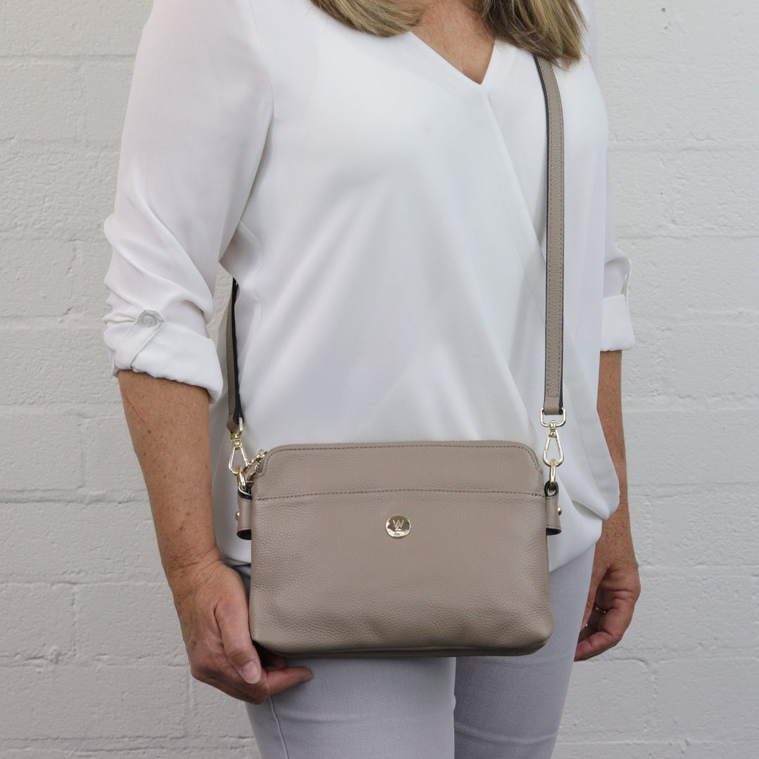 neutral taupe brown coloured curved bag with leather strap and gold hardware worn by model woman#colour_taupe